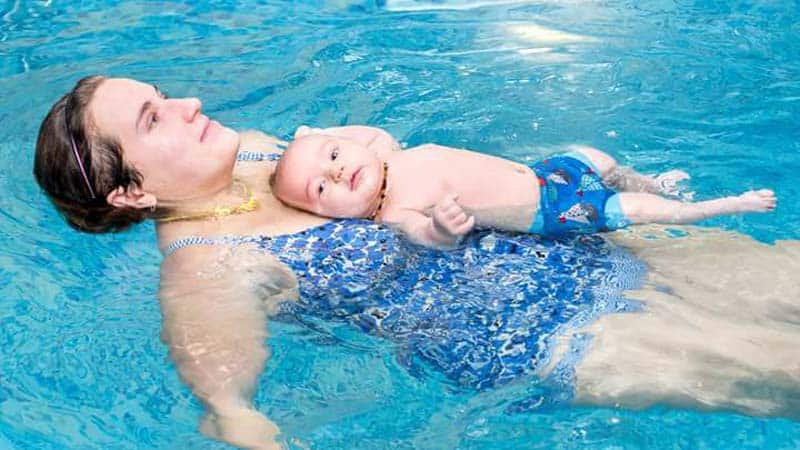 baby swimming lessons, mother in pool swimming with baby on her belly