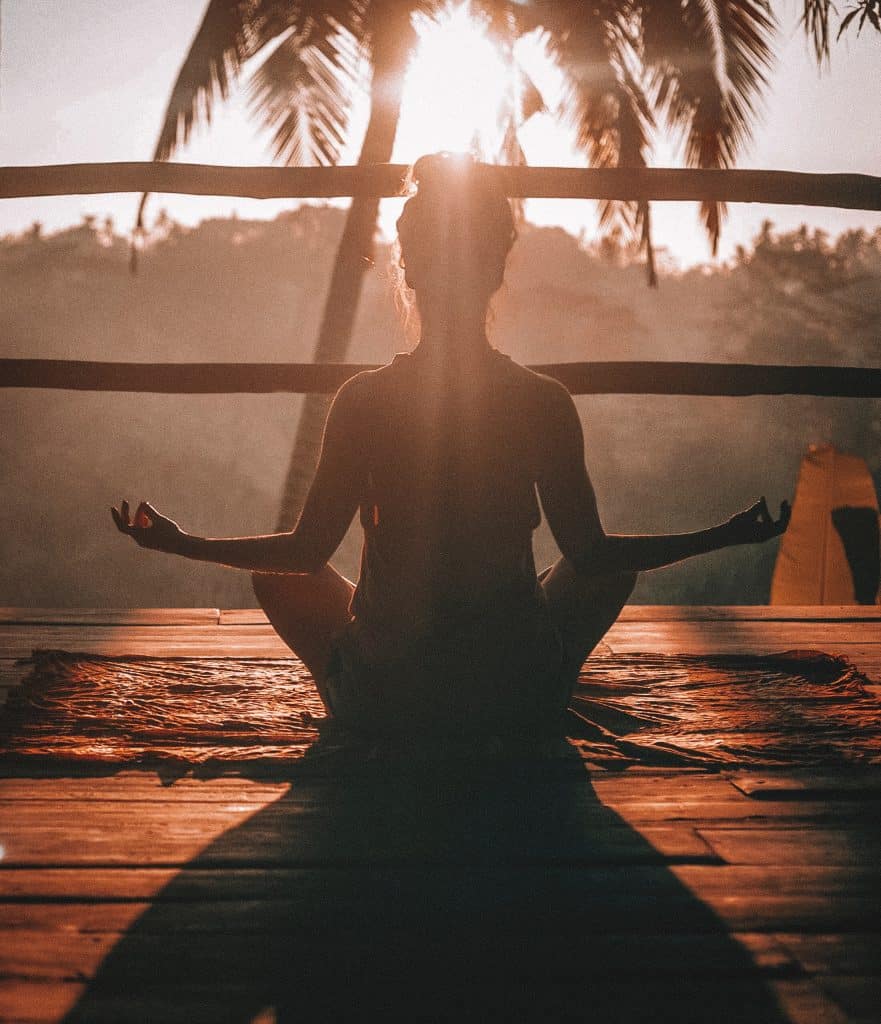 Woman meditating under palm tree in the setting sun